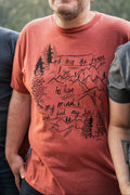 Person wearing a rust t-shirt with a nature-themed graphic and text.