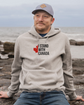 Man wearing a hoodie with 'I Stand With Canada' text and maple leaf graphic by the ocean.