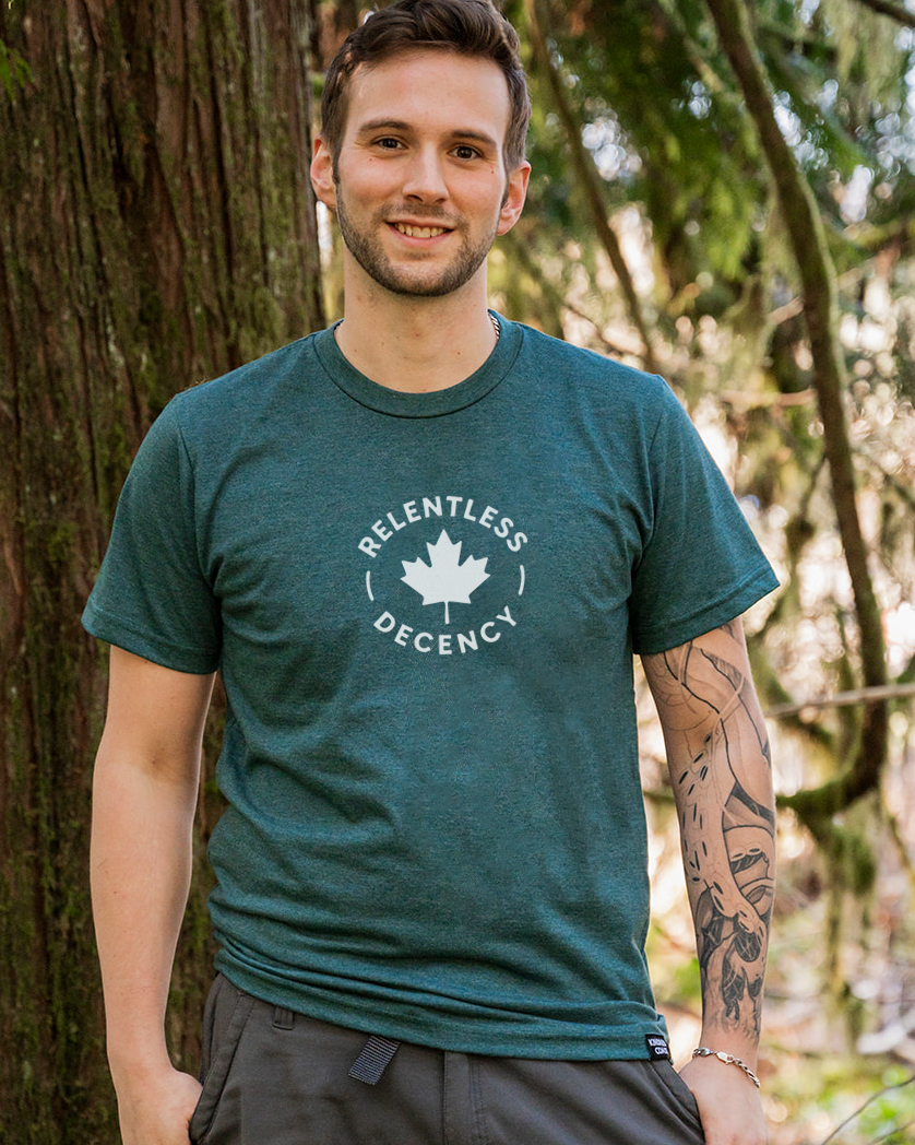 Man wearing a green t-shirt with a logo, standing next to a tree in a forest.