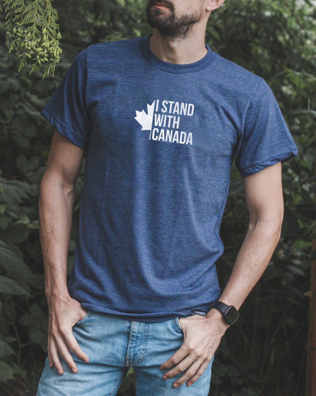 Man wearing a blue t-shirt with 'I Stand With Canada' text, standing outdoors among trees.